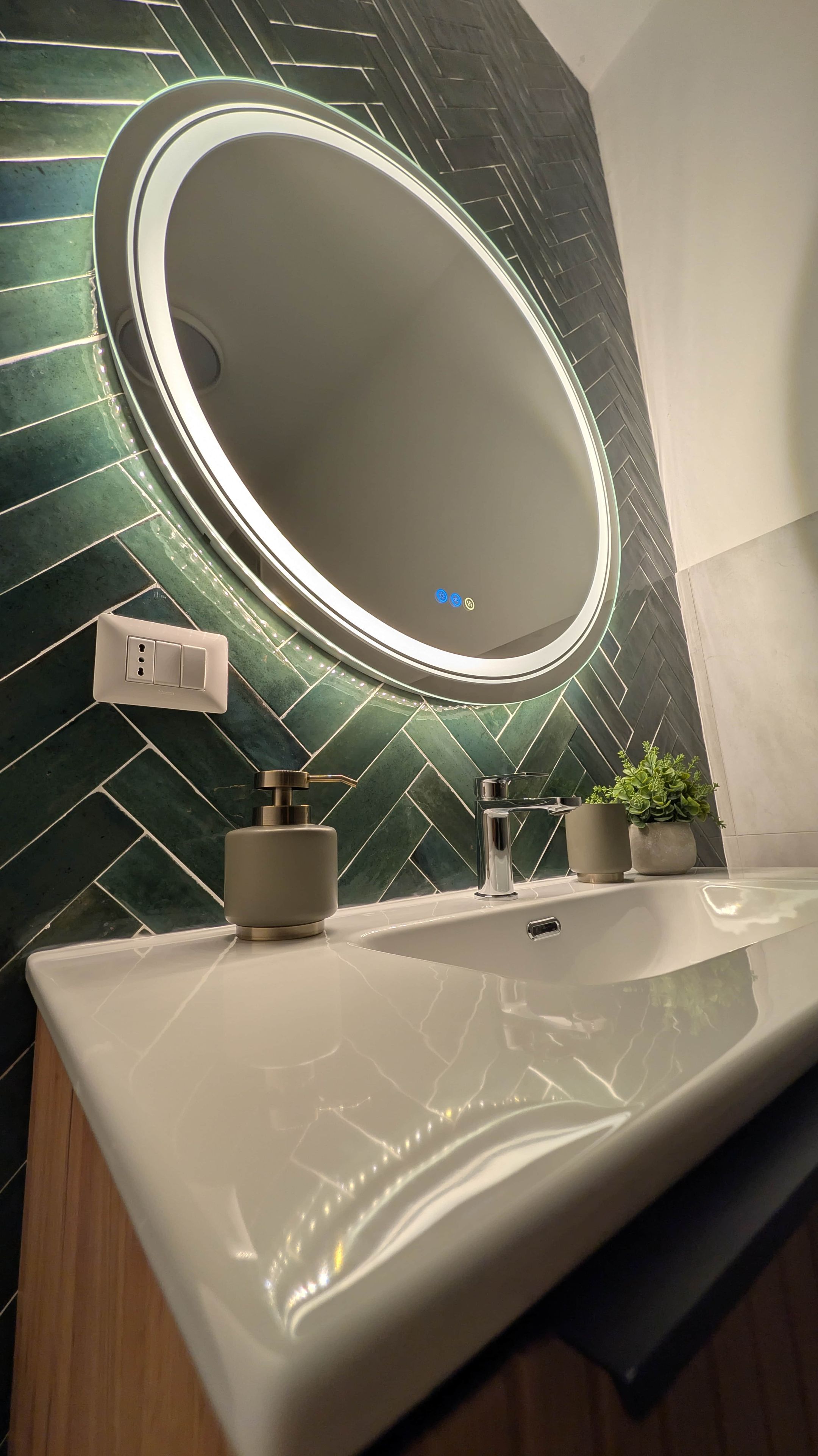 A bathroom with a modern sink, a mirror, and a green tiled wall.