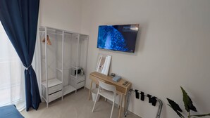 Ein Zimmer mit Schrank, Schreibtisch, Stuhl, Fernseher und einer Pflanze.