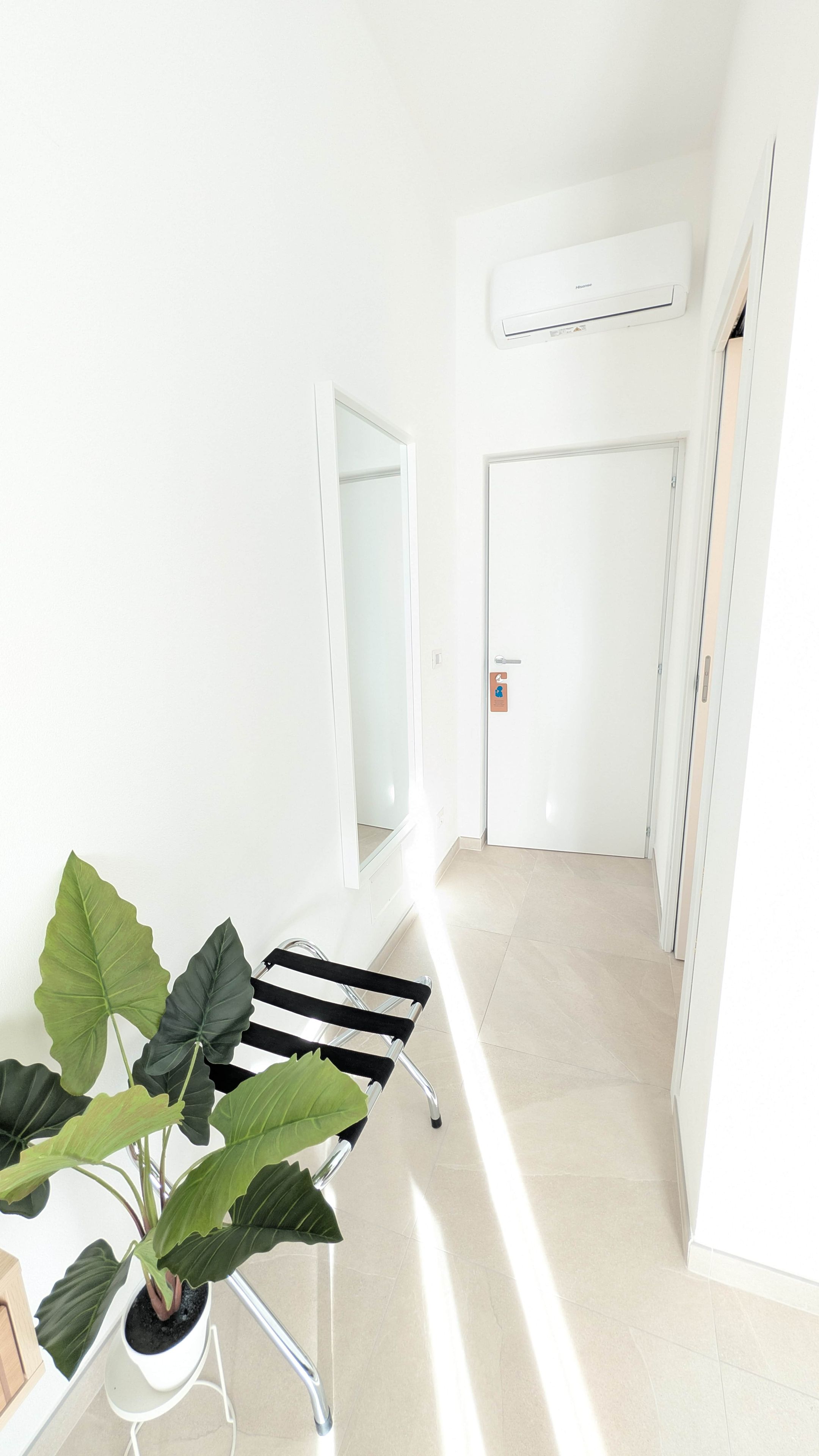 A bright hallway with a potted plant, a chair, and a door with a sign.