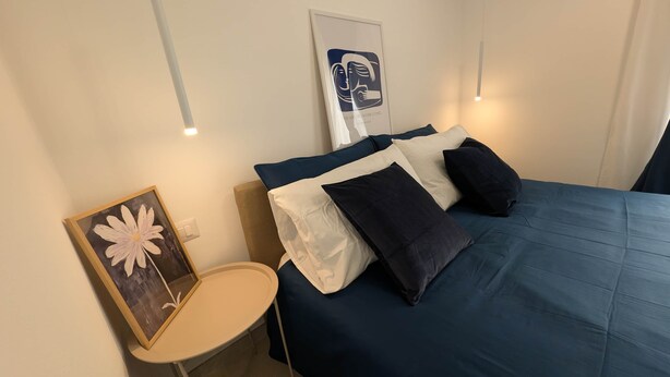 Ein Schlafzimmer mit einem Bett, Kissen, einem Nachttisch und einem Bilderrahmen.