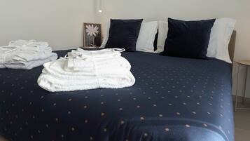 Un letto rifatto con una coperta blu scuro e asciugamani bianchi, un quadro appeso al muro e un comodino con una lampada.