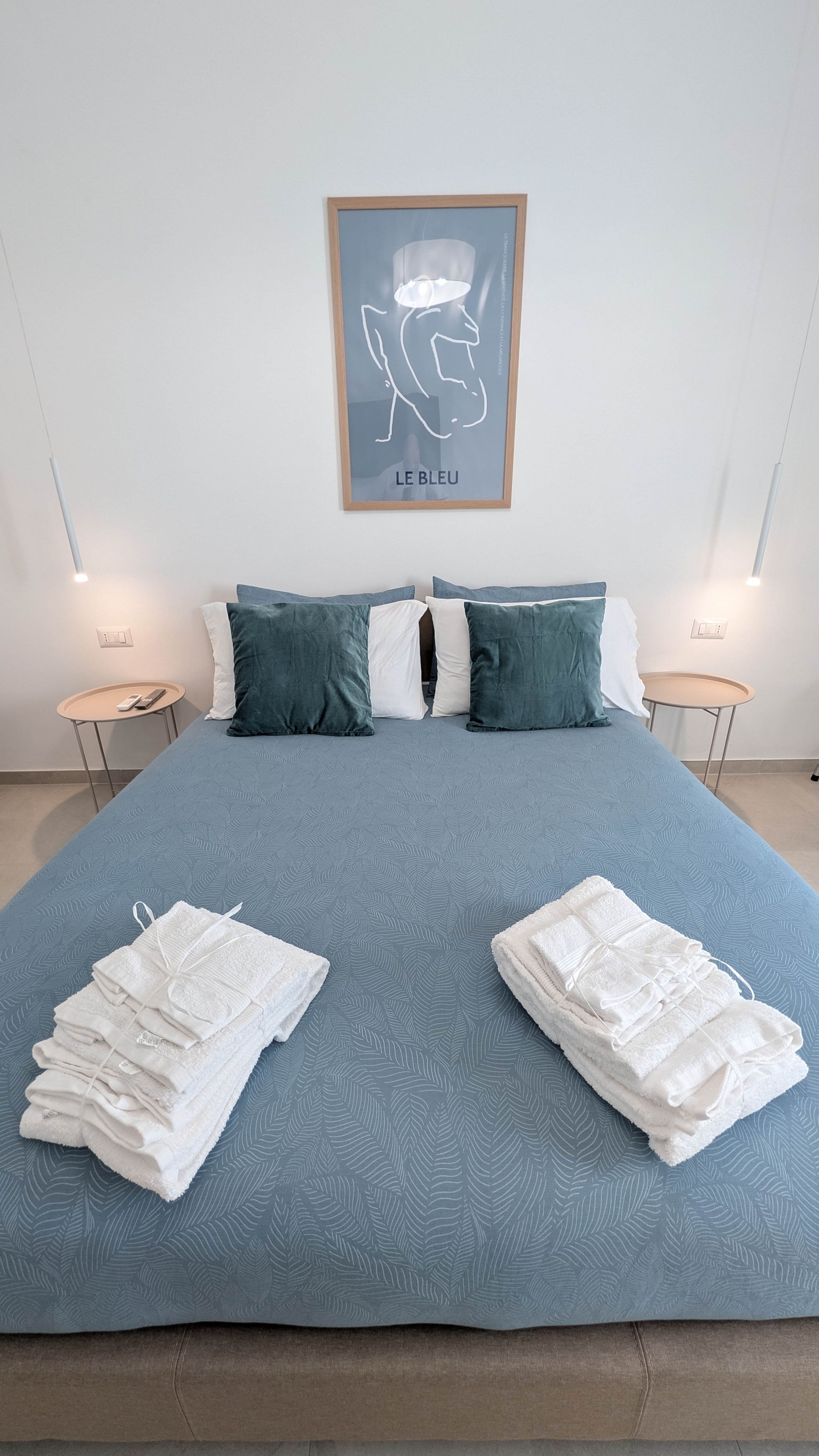 A neatly made bed with a blue patterned bedspread, two pillows, and a folded white towel on each side.