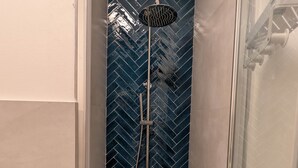 Ducha con diseño de mosaico de espiga, cabezal de ducha de mano y mampara de vidrio.