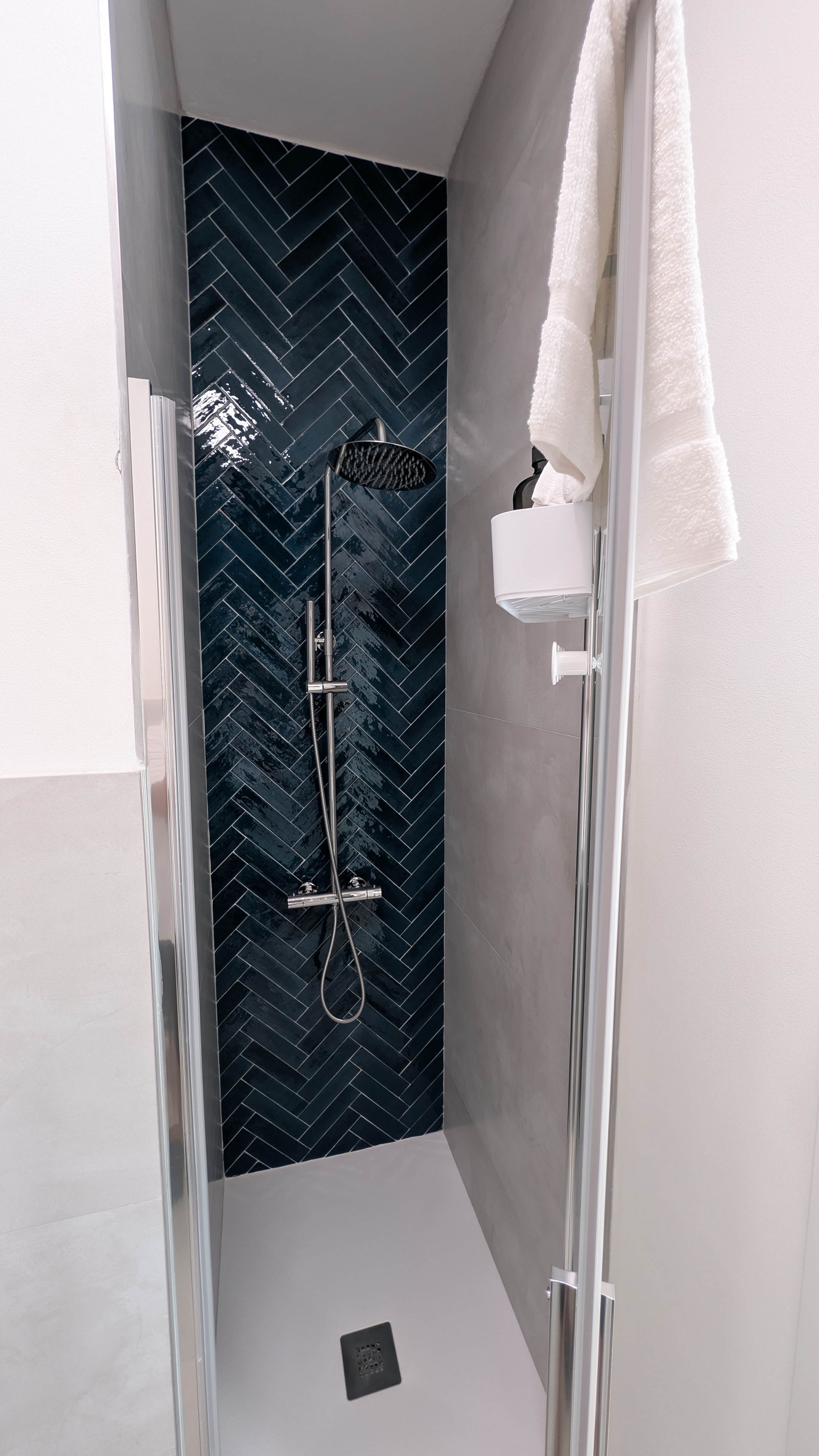 Eine moderne Dusche mit einem Zickzack-Fliesen-Spritzschutz, einer Handbrause und einem weißen Handtuch auf einem Halter.