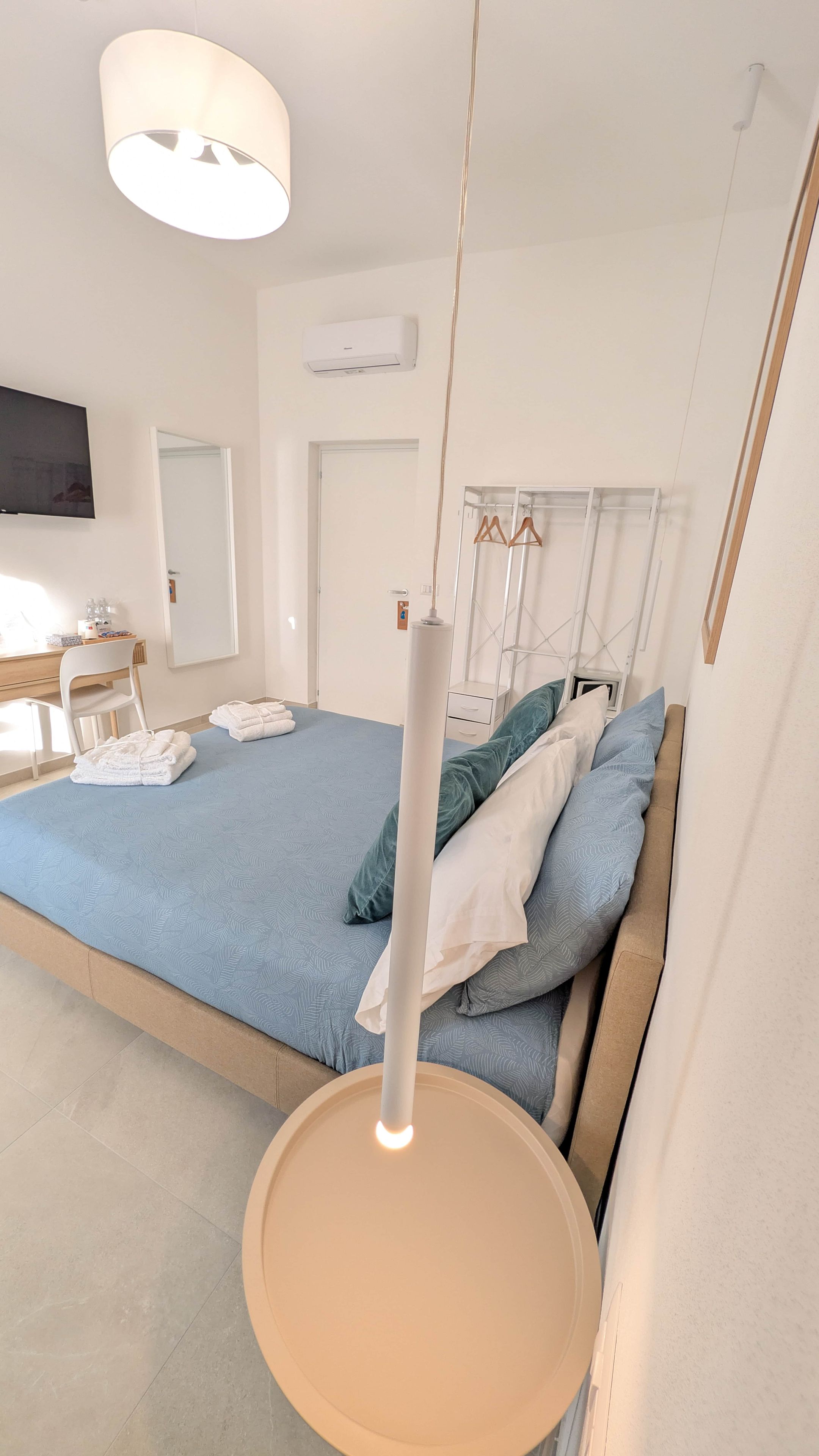 A bedroom with a bed, a hanging light fixture, a bedside table, a chair, and a TV.