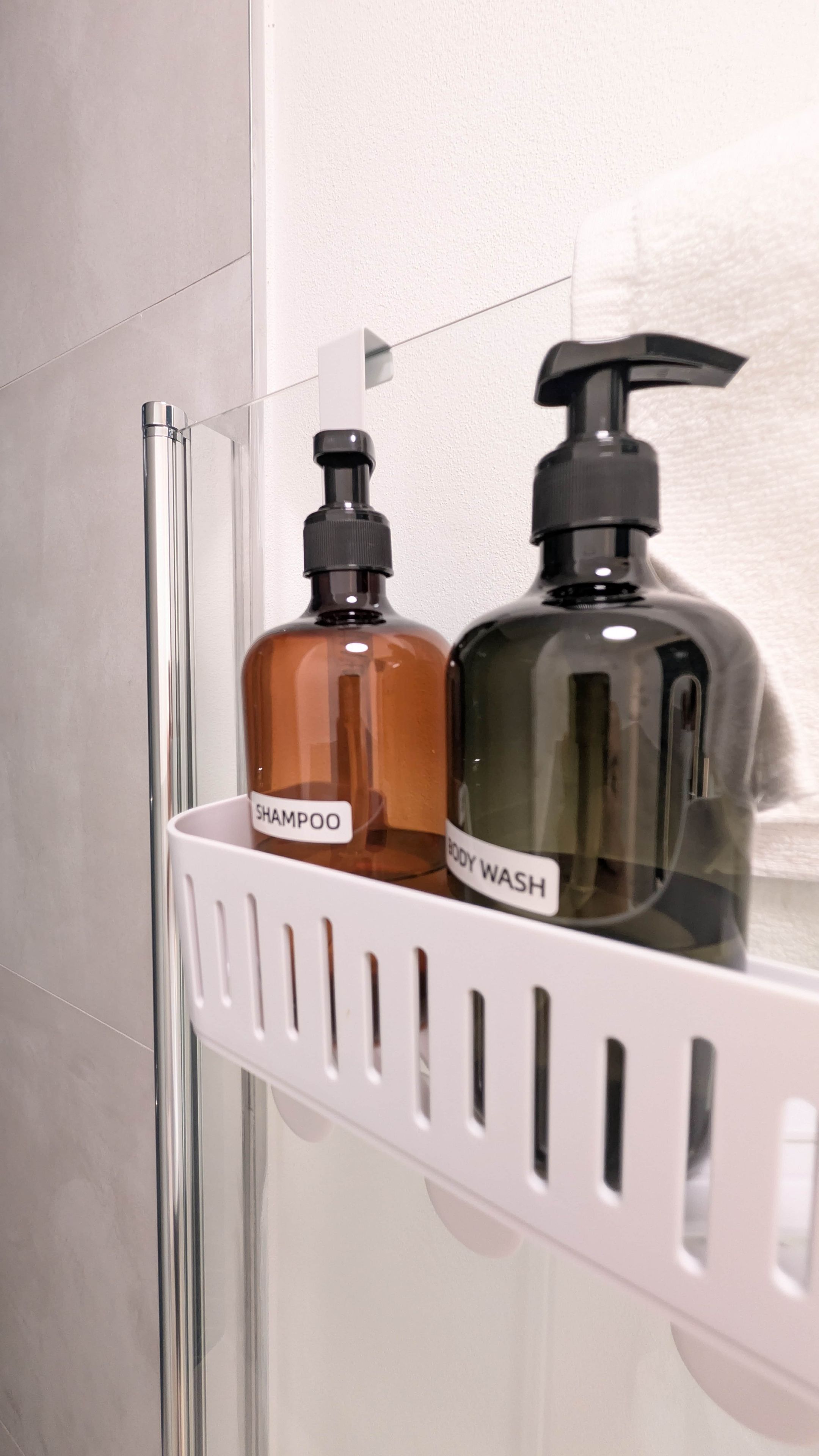 Un baño con un organizador blanco para ducha que contiene dos botellas de jabón líquido, una con la etiqueta 'SHAMPOO' y la otra 'BODY WASH'.