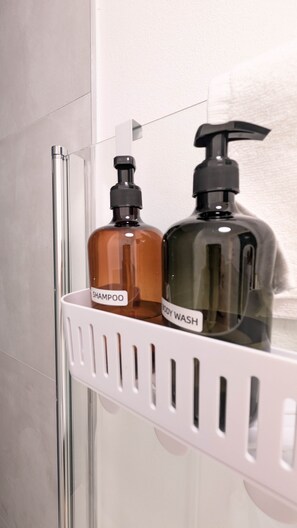 Ein Badezimmer mit einem weißen Duschorganisator, der zwei Flaschen Flüssigseife enthält, eine mit der Aufschrift 'SHAMPOO' und die andere 'BODY WASH'.
