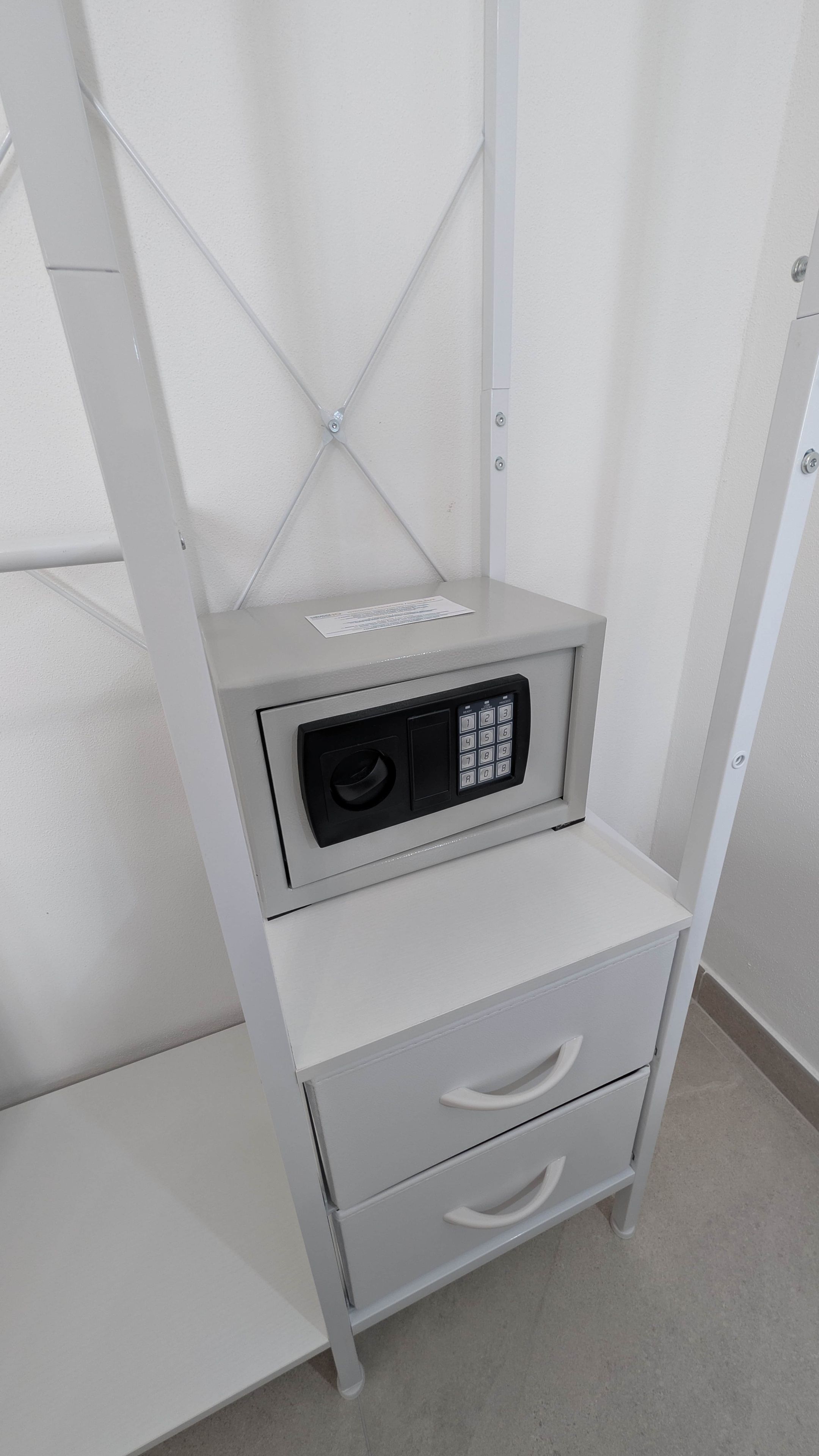 A white metal shelf unit with a built-in electronic device and a small drawer.