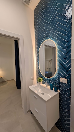 Et badeværelse med en hvid kommode, et spejl med lys og en blå backsplash med fiskebensmønster.
