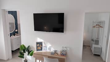 Una habitación de hotel moderna con cama, escritorio con silla, televisor de pantalla plana en la pared, espejo y armario con perchero.