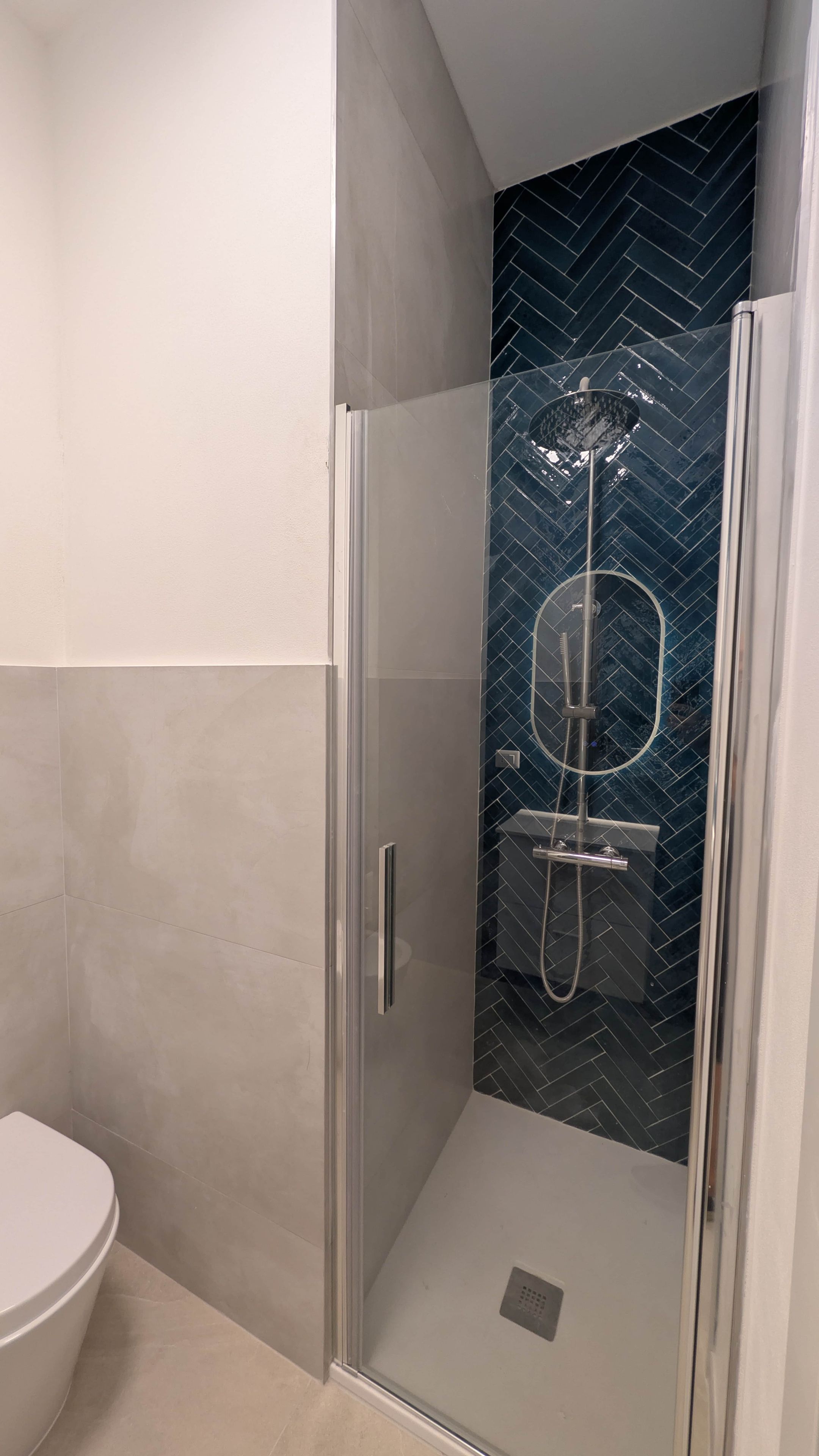 Een douche met glazen wanden en een achterwand van visgraatmozaïek.