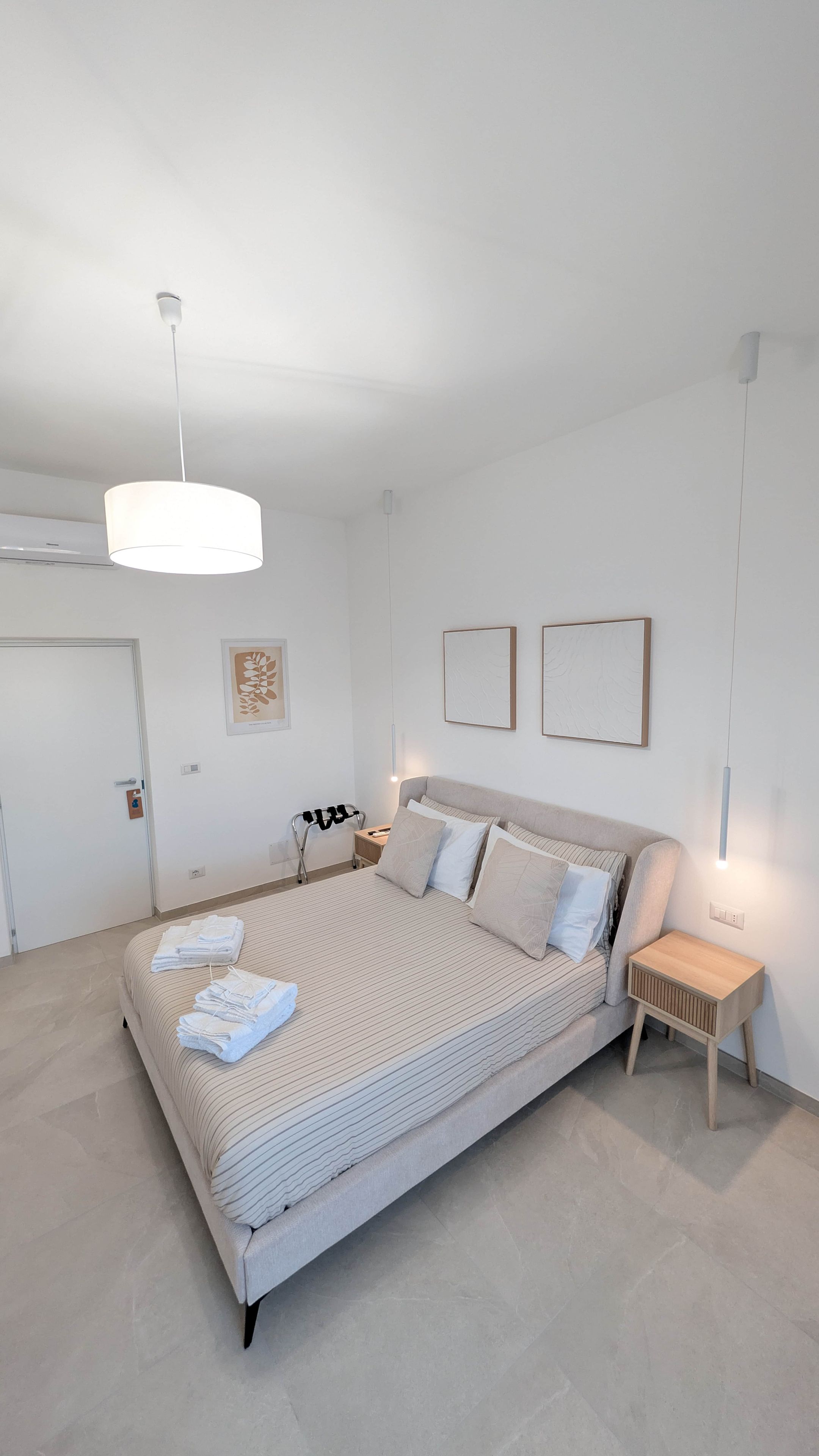 A modern bedroom with a large bed, bedside tables, a hanging light fixture, and artwork on the walls.
