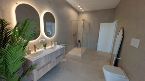 Ein modernes Badezimmer mit einem großen Spiegel, zwei Waschbecken, einer begehbaren Dusche und einer Toilette.