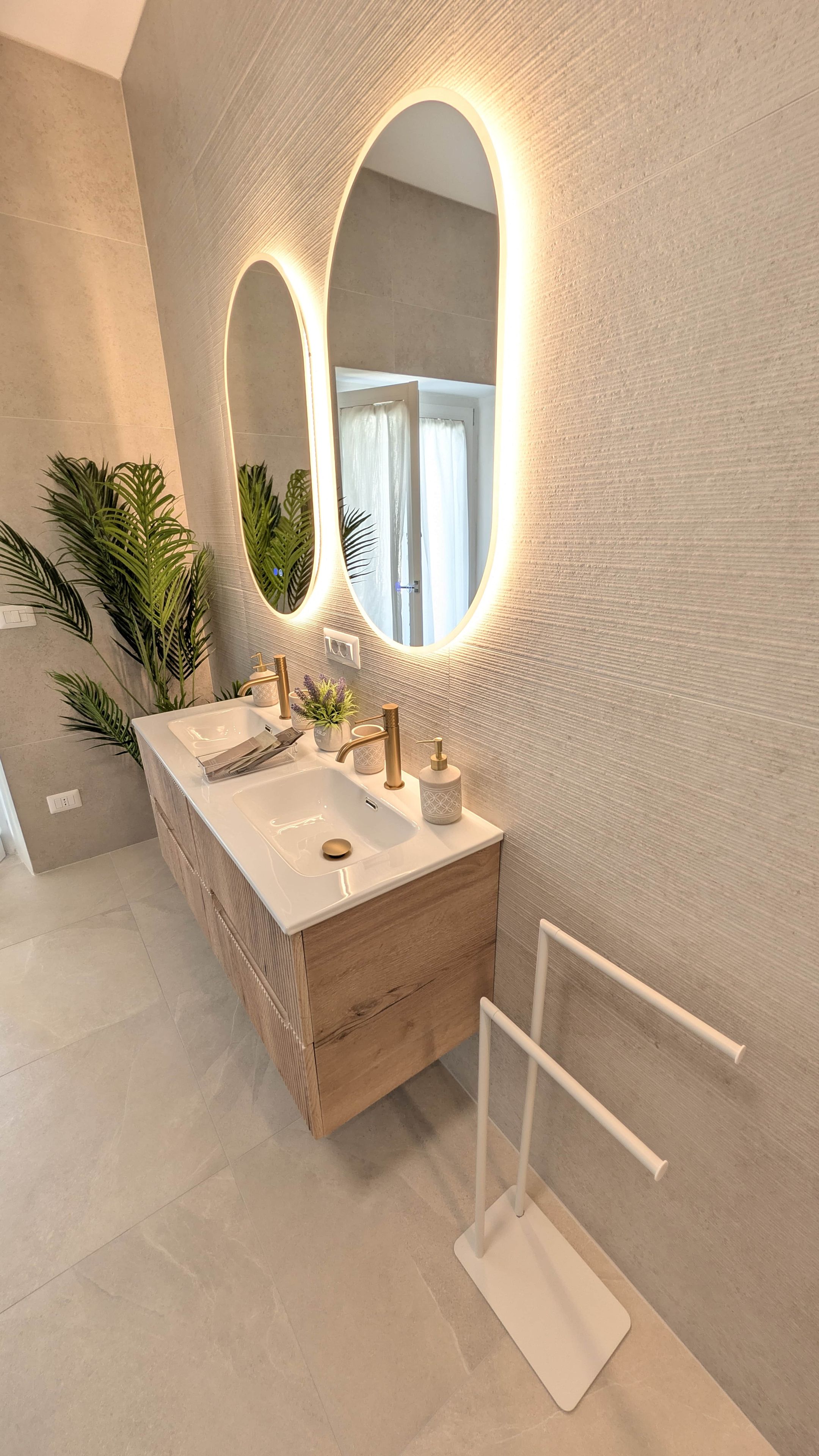 A modern bathroom with a double sink vanity, a large mirror with integrated lighting, and a white towel rack.