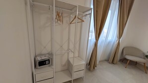 Ein weißer Kleiderschrank mit Bedienfeld, ein Sessel und ein Fenster mit Vorhängen.
