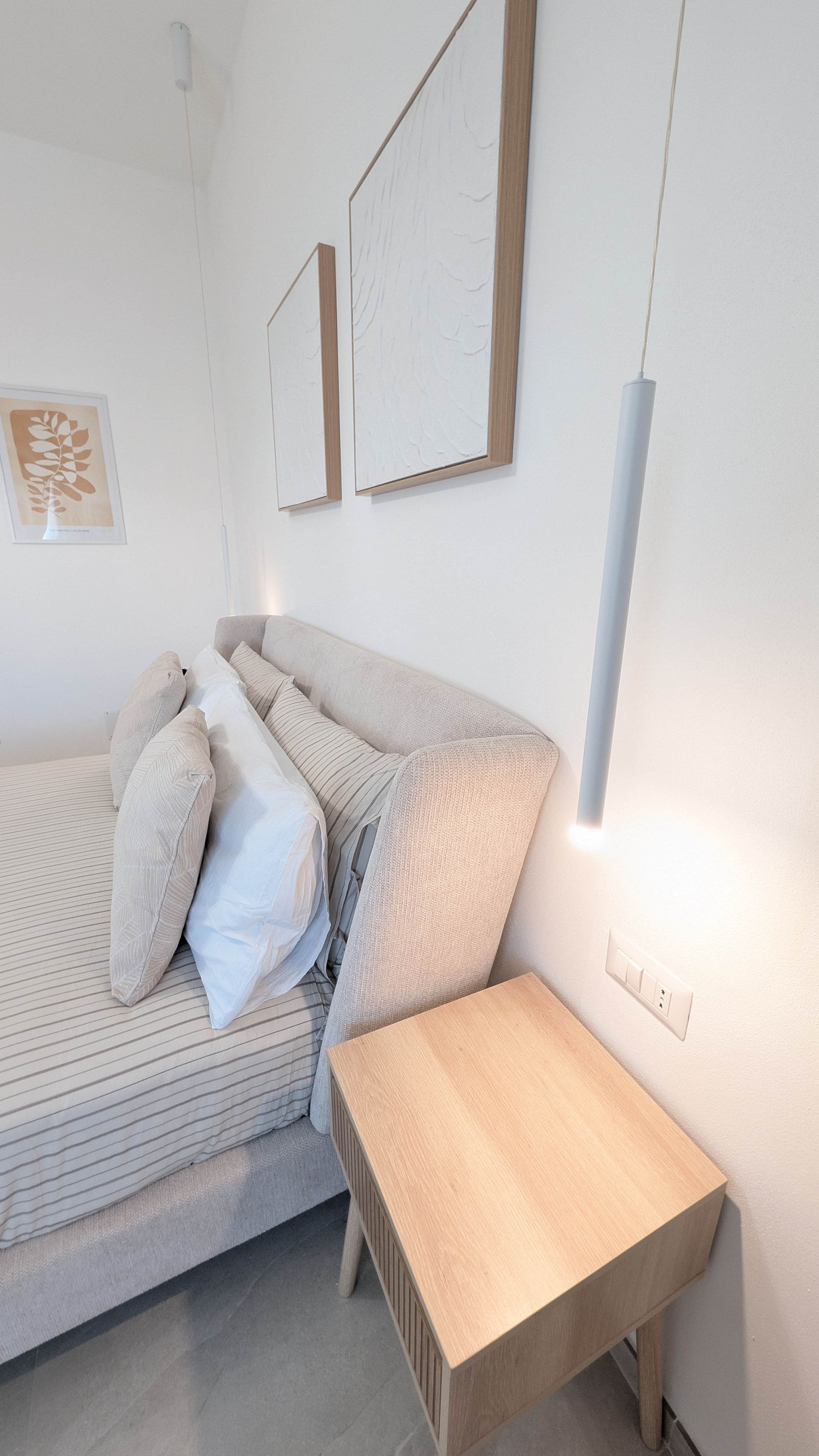 A bedroom with a bed, pillows, a bedside table, and wall-mounted artwork.