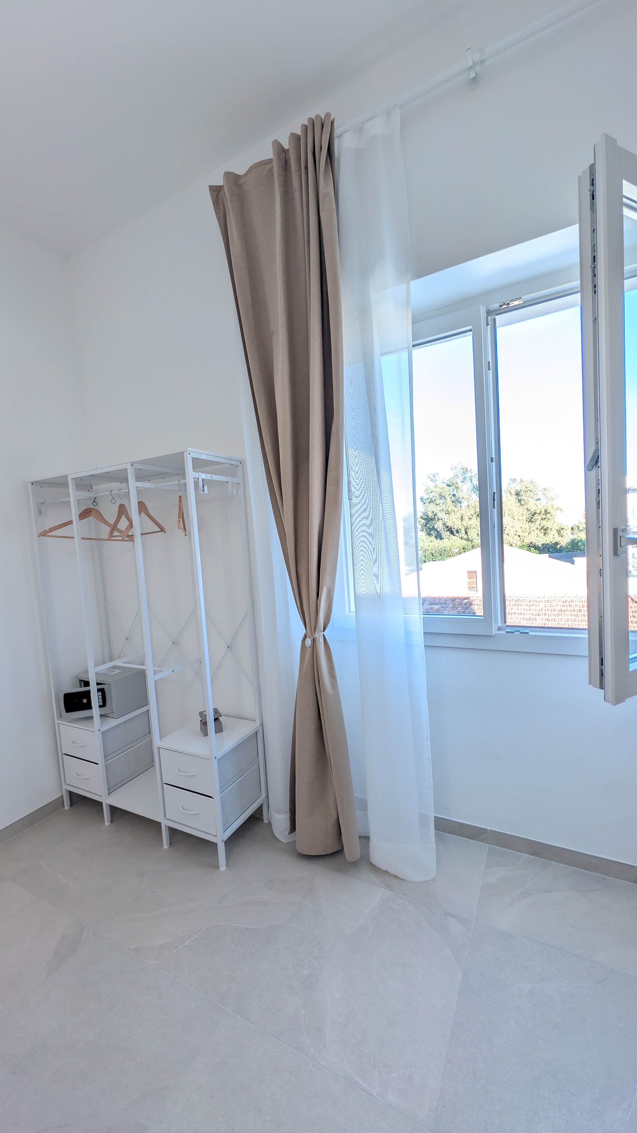 Une pièce dotée d’une grande fenêtre, d’une armoire avec espace pour suspendre des vêtements et d’une petite table sur laquelle se trouve un appareil.