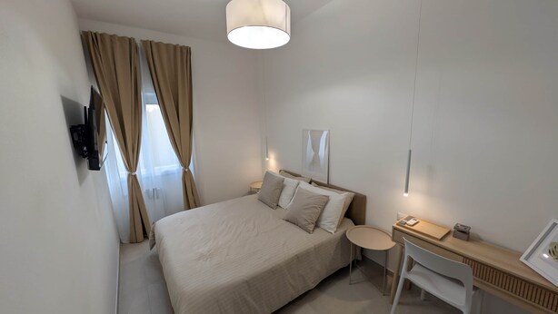 Une chambre d’hôtel équipée d’un lit, d’une table de chevet, d’un bureau et d’un téléviseur fixé au mur.