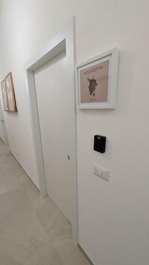Un pasillo con un mapa enmarco de Molarotto, una puerta y un dispositivo fijado a la pared.