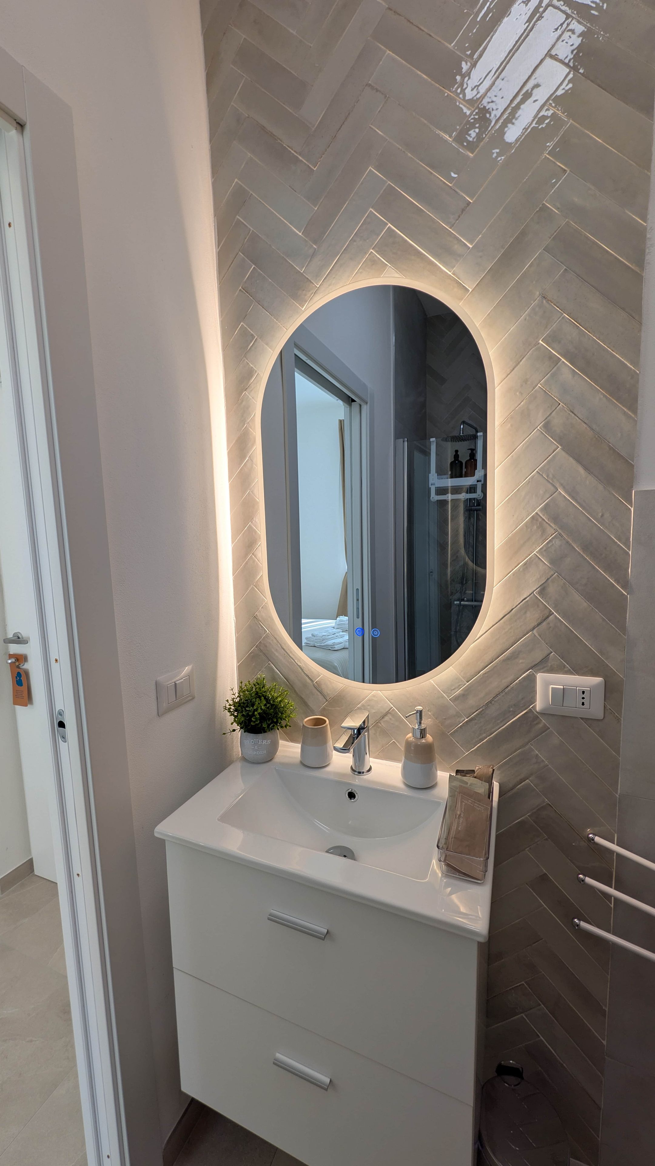 Un bagno con un mobile lavabo bianco, uno specchio illuminato e una parete con decorazione a spina di pesce.