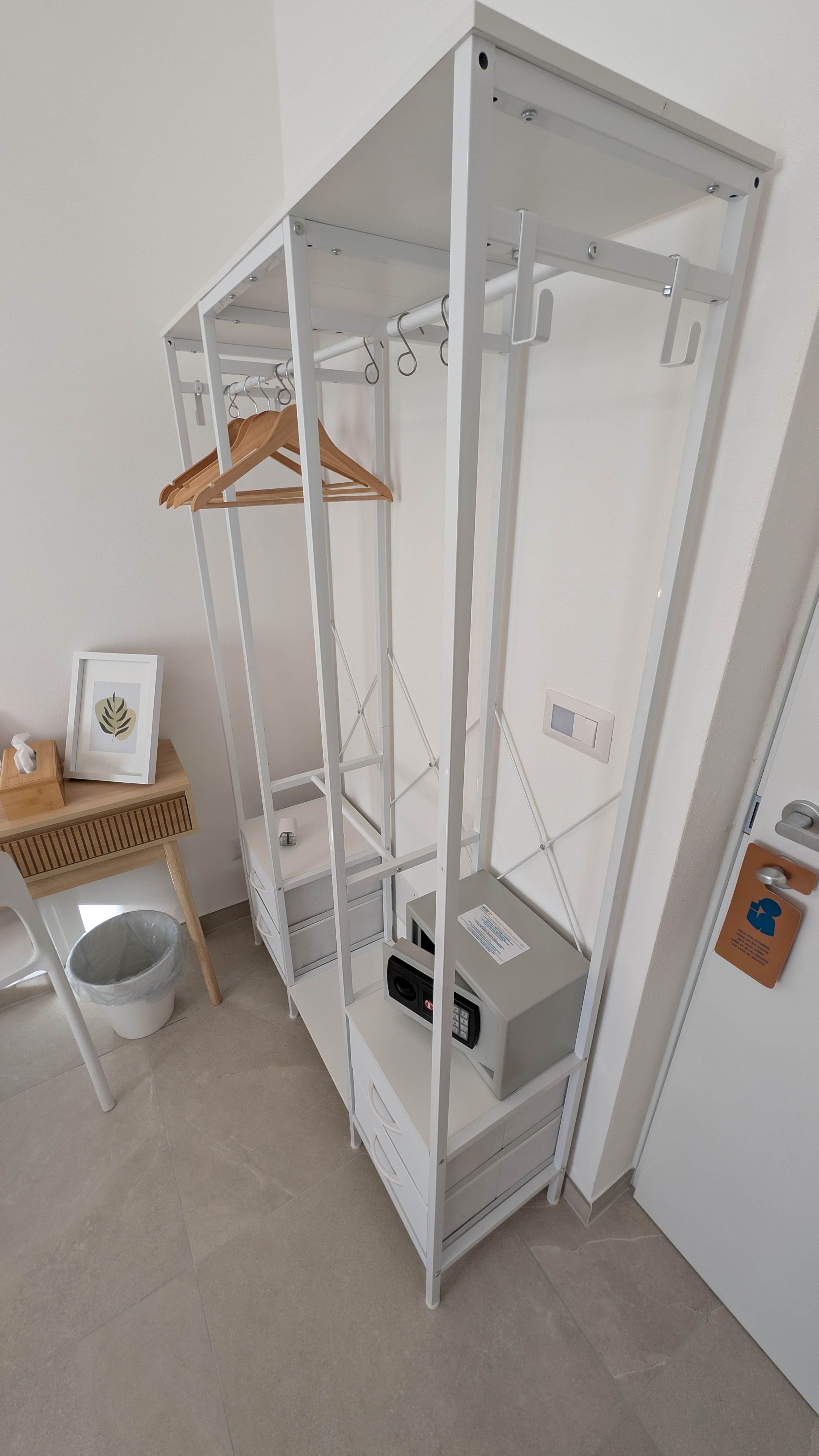 Habitación compacta con armario empotrado, una pequeña mesa con un marco de fotos y un cubo de basura.