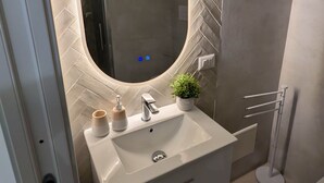 Une salle de bain moderne avec un mur orné d’un motif en chevrons, un miroir rond, un lavabo blanc et une petite plante en pot.