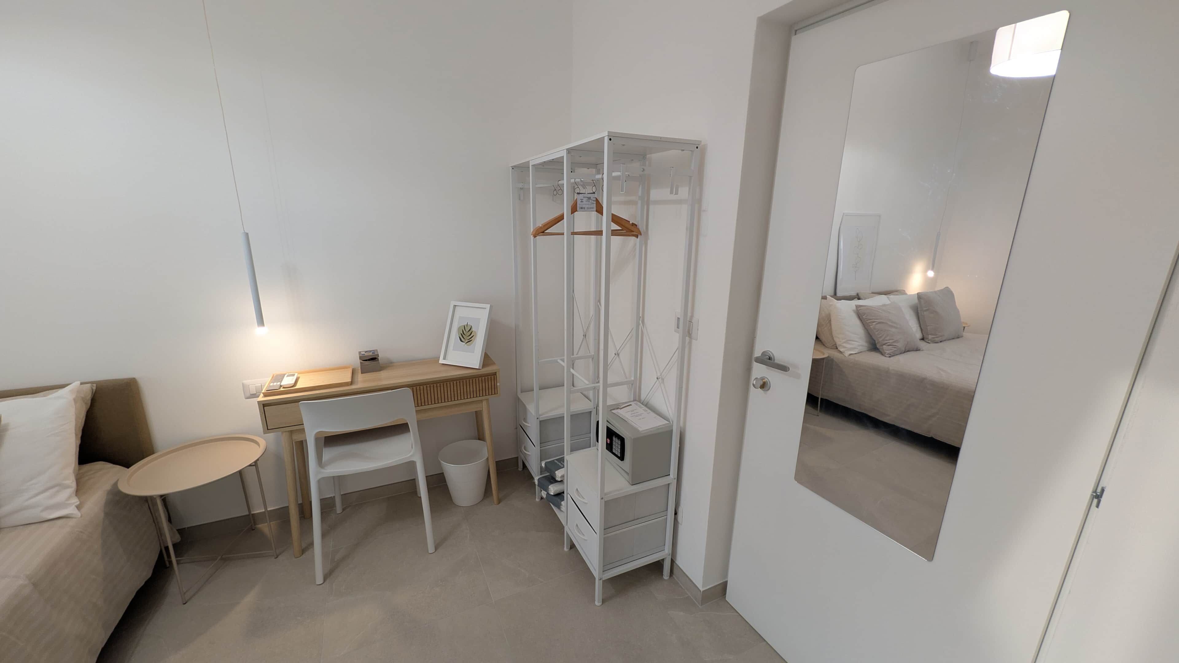 Una camera da letto compatta con un letto, una scrivania, una sedia, un armadio e uno specchio.