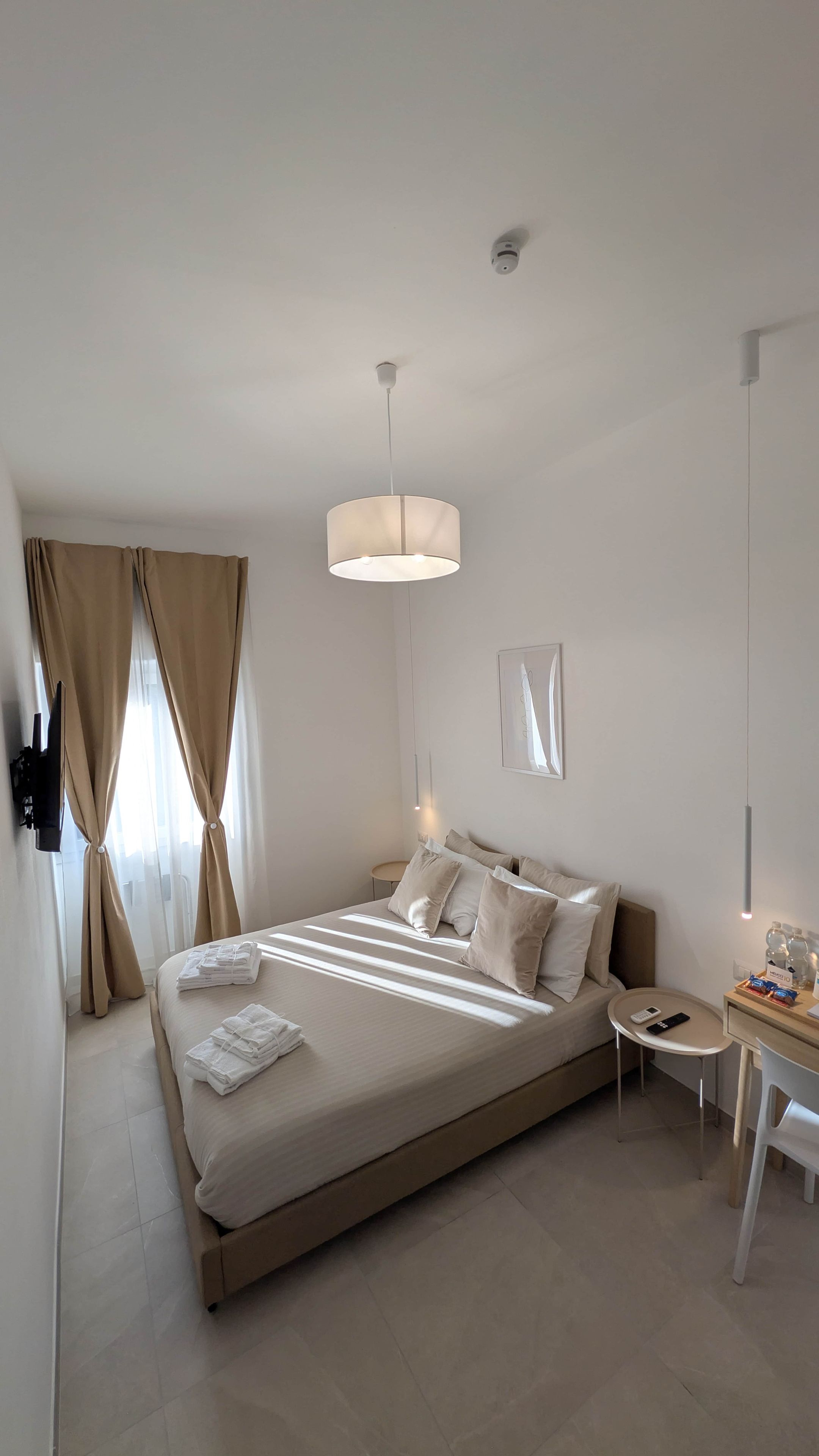 Une chambre d’hôtel moderne avec un grand lit, des tables de chevet, un bureau et un luminaire suspendu.
