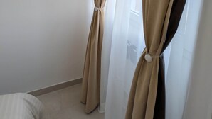 Une pièce avec des rideaux beiges noués en bas, un lit blanc et un mur uni.