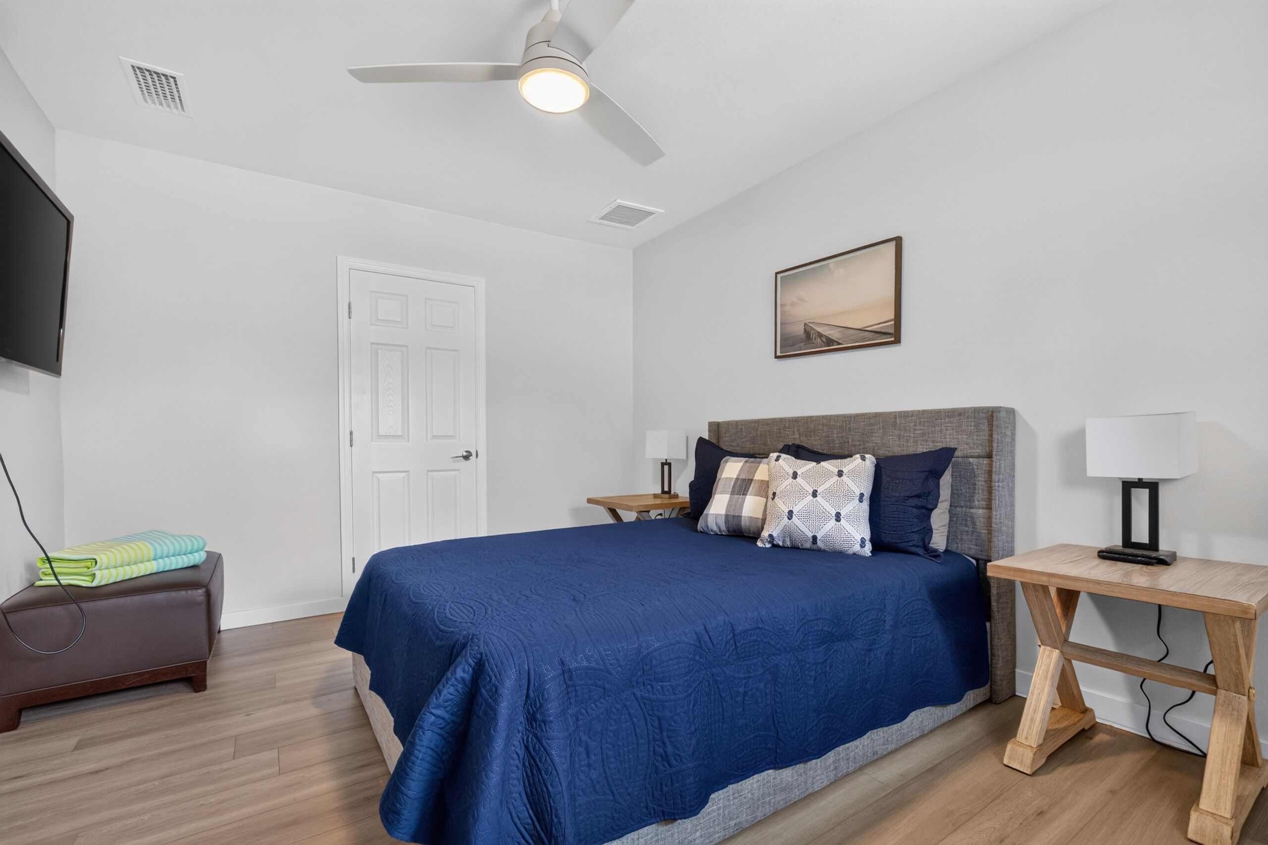 A bedroom with a bed, bedside tables, a desk, a chair, a TV, and a ceiling fan.