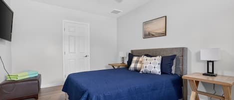 A bedroom with a bed, bedside tables, a desk, a chair, a TV, and a ceiling fan.