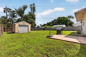 A residential backyard with a garage, a small shed, a barbecue grill, and a paved patio area. - Charming 2-Bedroom Home Near Siesta Key, Sleeps 6 (Sarasota)