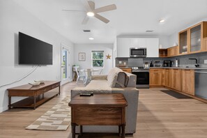 A modern living room with a flat-screen TV, a sofa, a coffee table, and a ceiling fan. - Charming 2-Bedroom Home Near Siesta Key, Sleeps 6 (Sarasota)