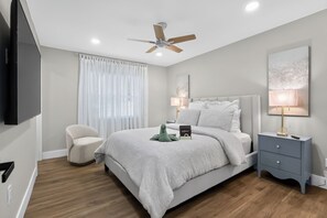 A bedroom with a bed, a chair, a nightstand, a lamp, a ceiling fan, and a TV. - 3-bedroom house in beautiful St. Cloud with cool AC breeze (St. Cloud)