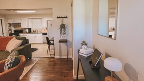 Een moderne woonkamer met een donker houten vloer, een bank met kussens, een salontafel met een laptop en een lamp, en uitzicht op de keuken.