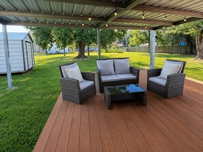Eine Terrasse im Freien mit Korbmöbeln, einem Glastisch und einer Metall-Dachkonstruktion.