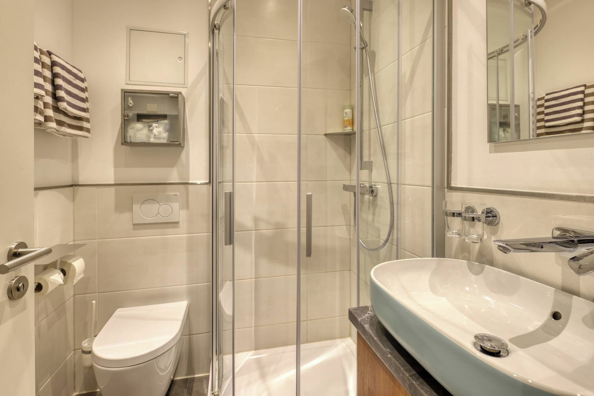 A modern bathroom with a glass-enclosed shower, a white toilet, and a large sink with a marble countertop.