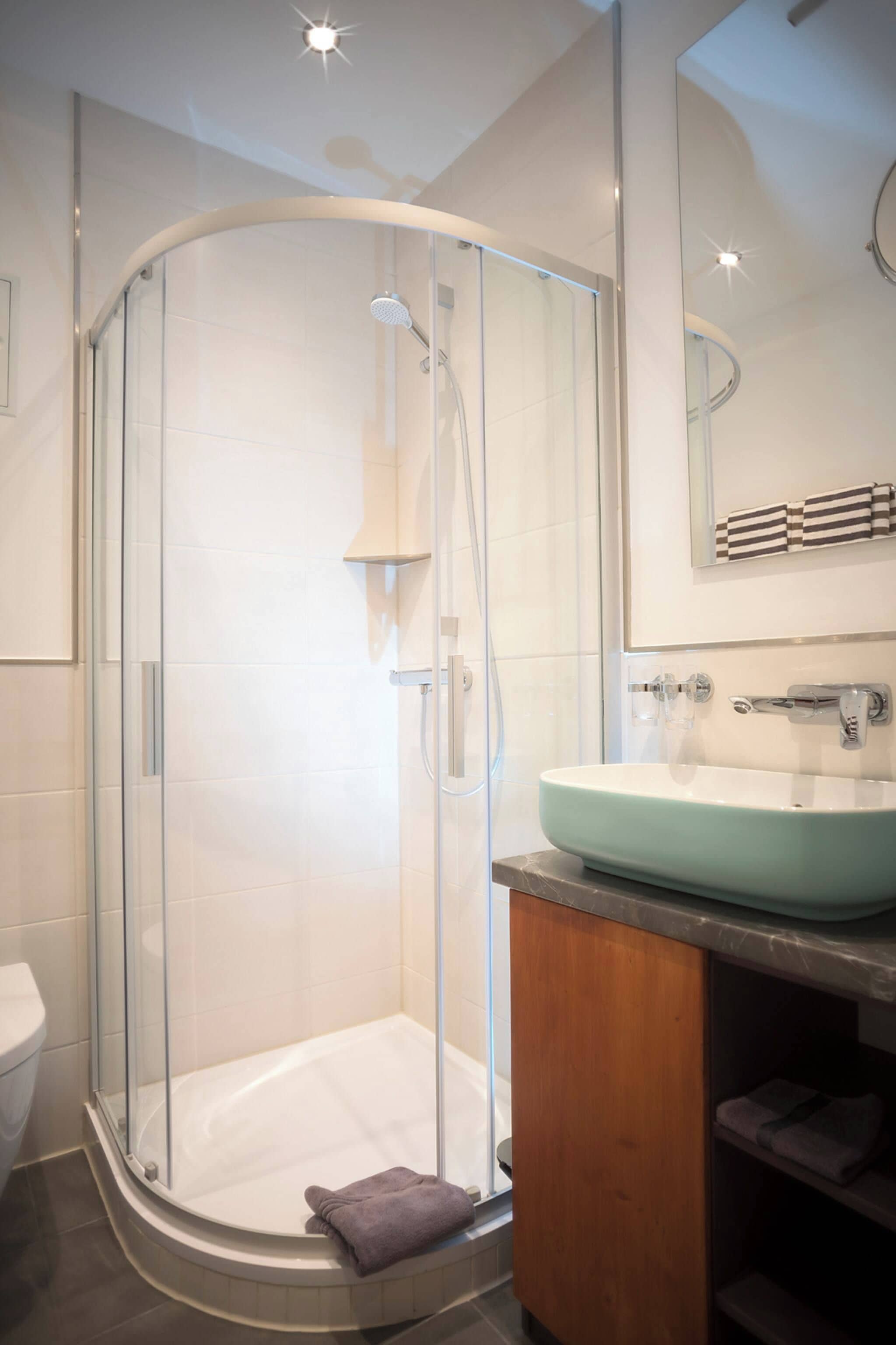 Un bagno moderno con doccia vetro, lavabo con piano in marmo e specchio sopra il lavabo.