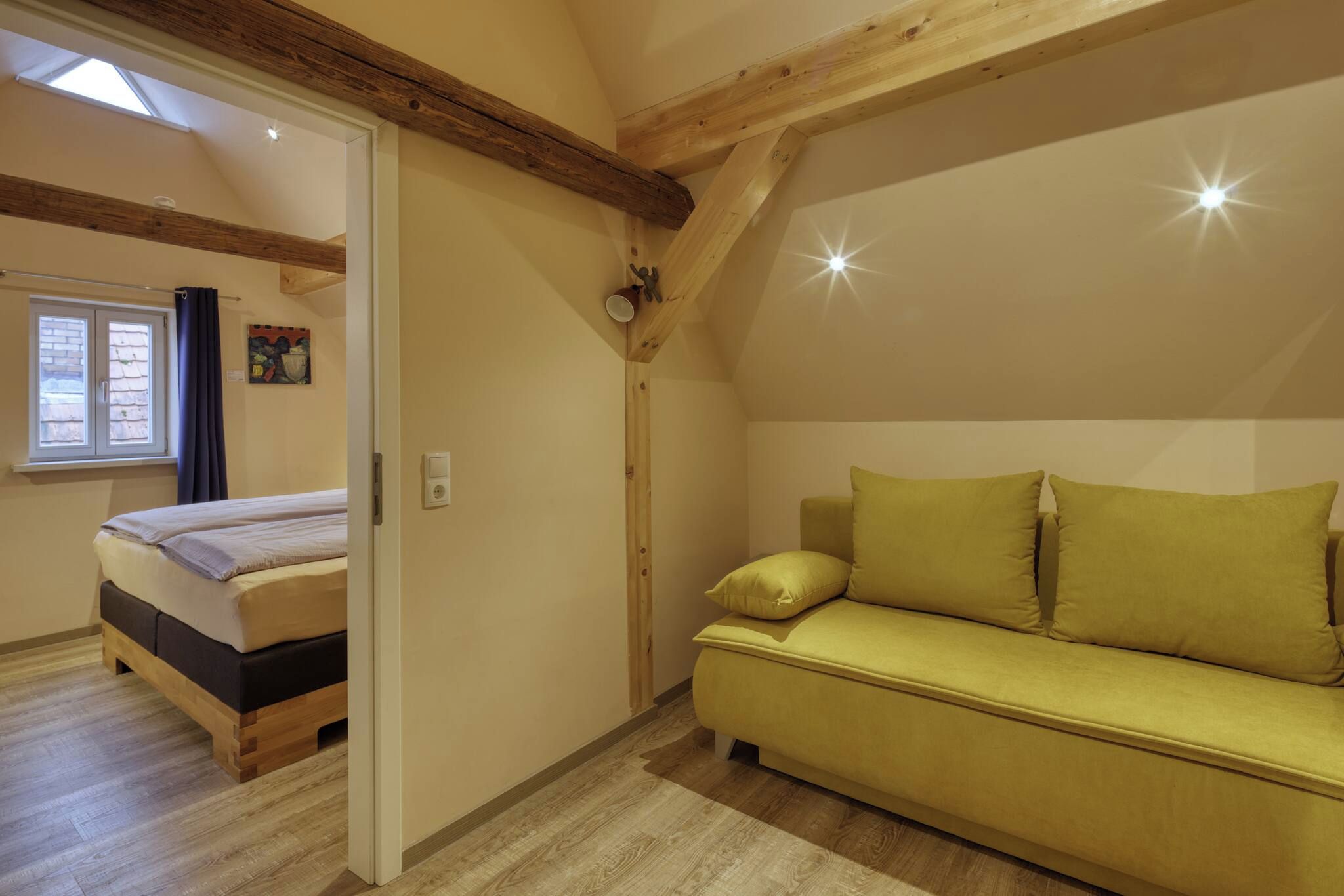 A bedroom with a bed, a sofa, a skylight, and a window.