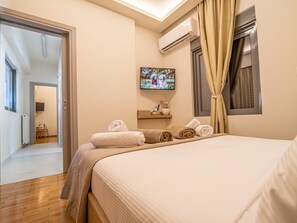 Una habitación de hotel con una cama, un televisor fijado a la pared, una ventana con cortinas y una puerta que da a otra habitación.