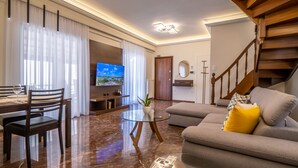 Uma sala de estar moderna com televisão de tela plana, área de jantar com mesa e cadeiras, sofá com almofadas e uma escada.