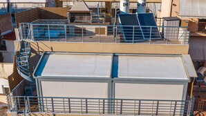 A multi-story building with a rooftop terrace featuring a metal staircase and a flat roof with a white awning. - Nuvion (Athens)