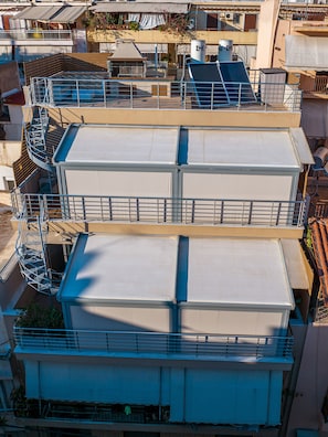 A multi-story building with a rooftop terrace featuring a metal staircase and a flat roof with a white awning. - Nuvion (Athens)