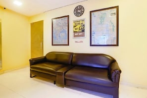 Una habitación con un sofá de cuero marrón, un reloj de pared y dos mapas enmarcados.