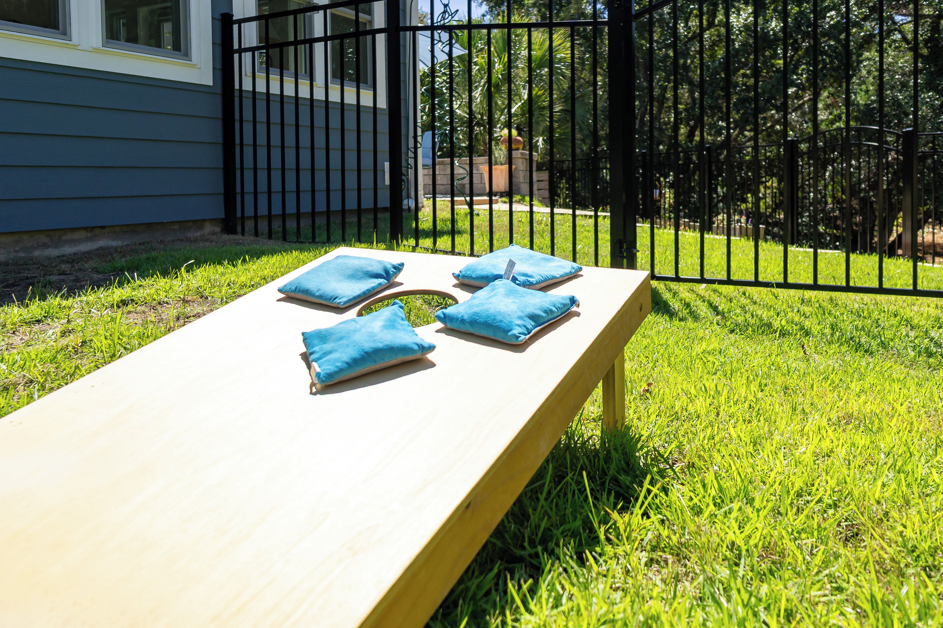 A wooden bench with blue cushions in a grassy outdoor area, surrounded by a black metal fence.