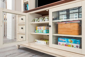 Ein Kinderzimmer mit einem weißen Schrank voller Spielzeug und Gesellschaftsspielen, einem Korbwäschekorb und einem Samsung Fernseher.