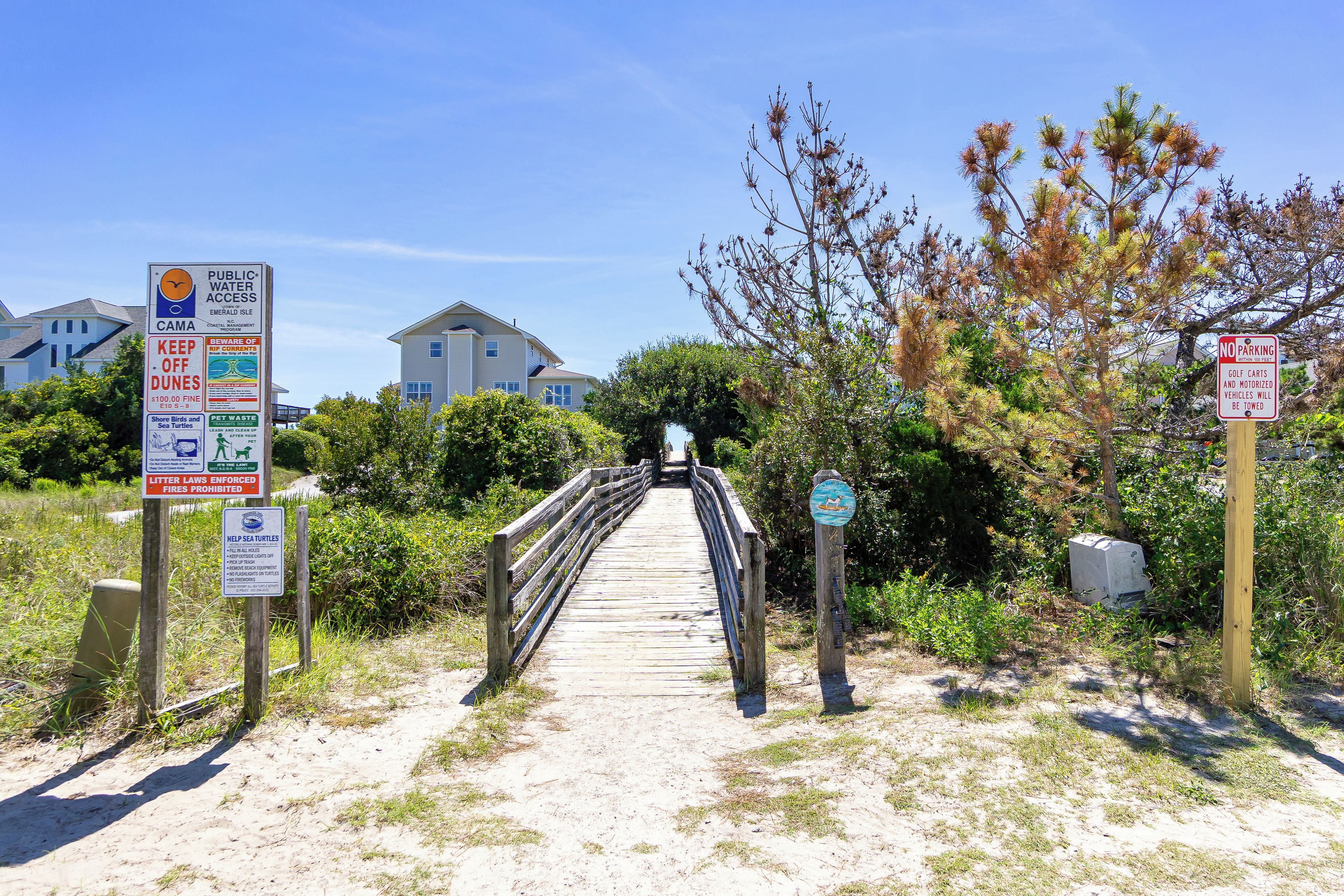 A wooden boardwalk leading to a building with multiple signs, including one about public water access and another about no parking.