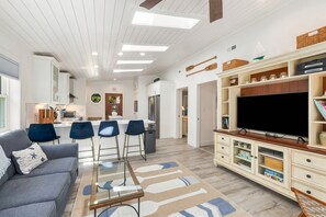Un salon moderne avec un canapé gris, des fauteuils bleus, une table basse en verre, un téléviseur à écran plat et un meuble de rangement en bois.