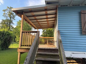 Une terrasse en bois surmontée d’un toit en métal, qui mène à une maison dont le revêtement extérieur est bleu.