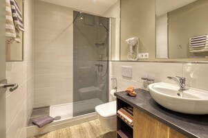 Un baño moderno con ducha de vidrio, un lavamanos blanco y un tocador con espejo.